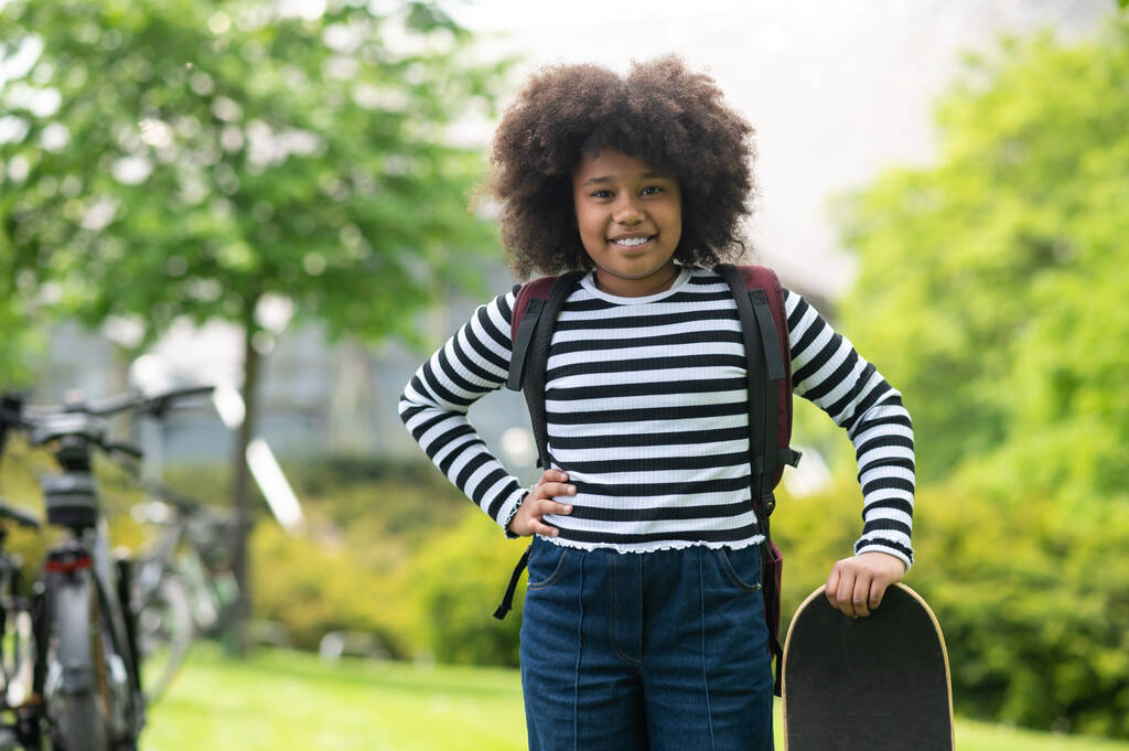 Молода дівчина весело стоїть зі скейтбордом влітку на відкритому повітрі школярка насолоджується скейтбордингом в парку. - Фото, зображення