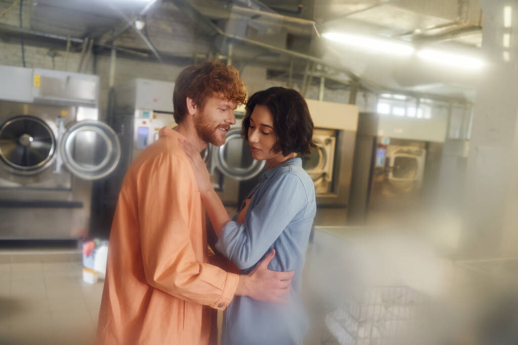 veselý ryšavý muž objímání mladý asijské přítelkyně v rozmazané veřejné prádelna - Fotografie, Obrázek