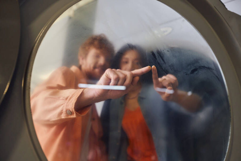 zamazana młoda romantyczna para dotykająca szklanki pralki w publicznej pralni - Zdjęcie, obraz