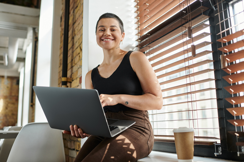 happy tattooed woman using laptop, sitting on windowsill, coffee to go, startup project, coworking - Photo, Image