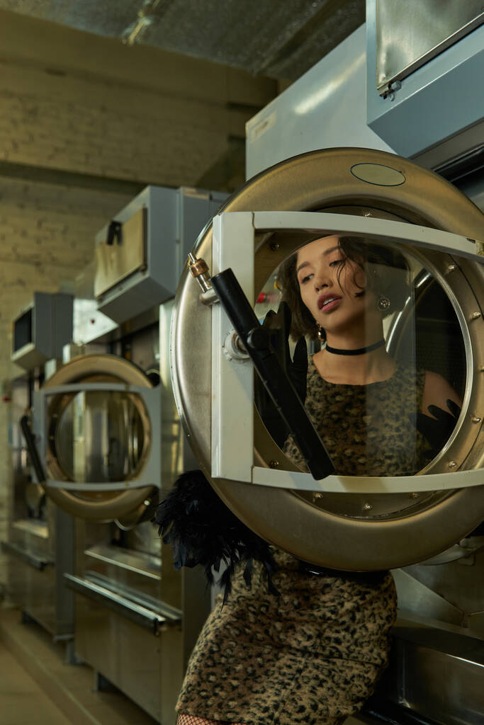 stylový mladý asijské žena v šaty pózovat v blízkosti dveří pračky v praní mincí - Fotografie, Obrázek