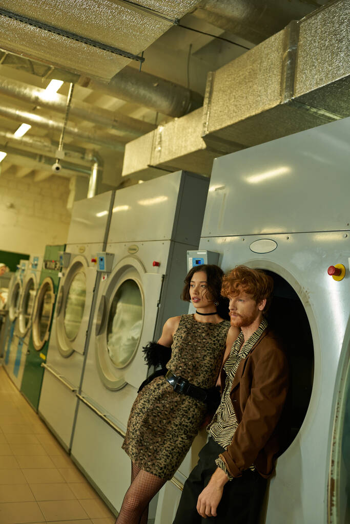 moda joven pareja multiétnica en trajes modernos posando en la lavandería pública por la noche - Foto, imagen