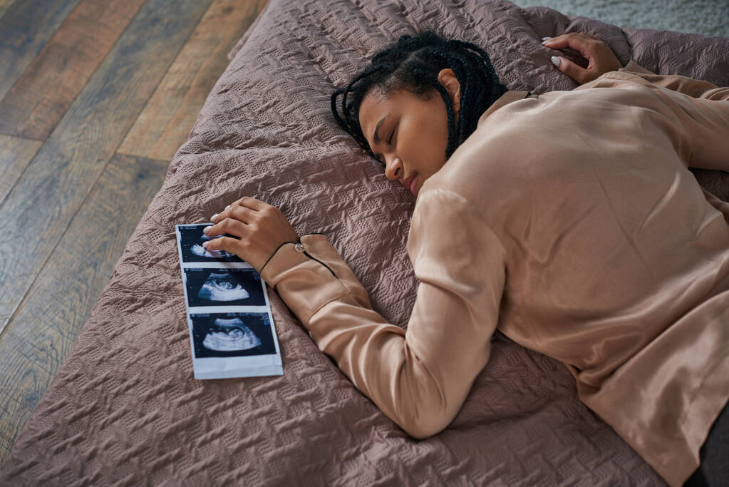вид сверху на беспокойную африканскую американку лежащую на кровати возле ультразвука, нерожденного ребенка, аборт - Фото, изображение