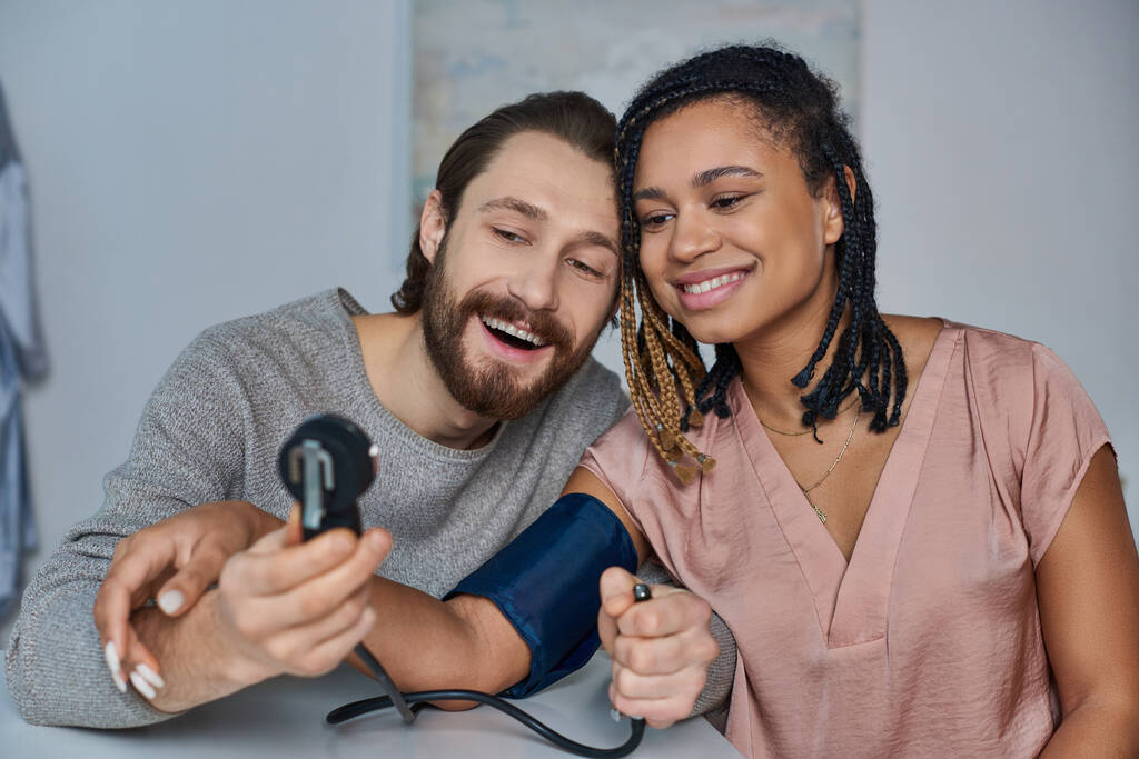 joyful man measuring blood pressure of pregnant african american wife, future parents, happiness - Photo, Image