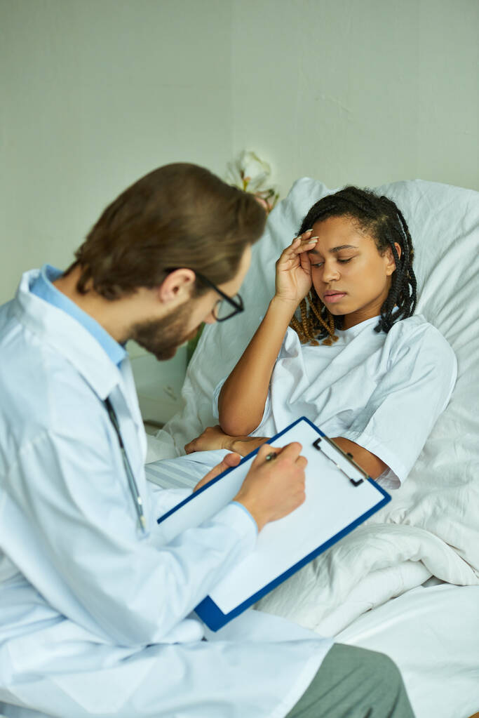 врач в очках выписывает рецепт обеспокоенной африканской женщине, частной палате, больнице - Фото, изображение