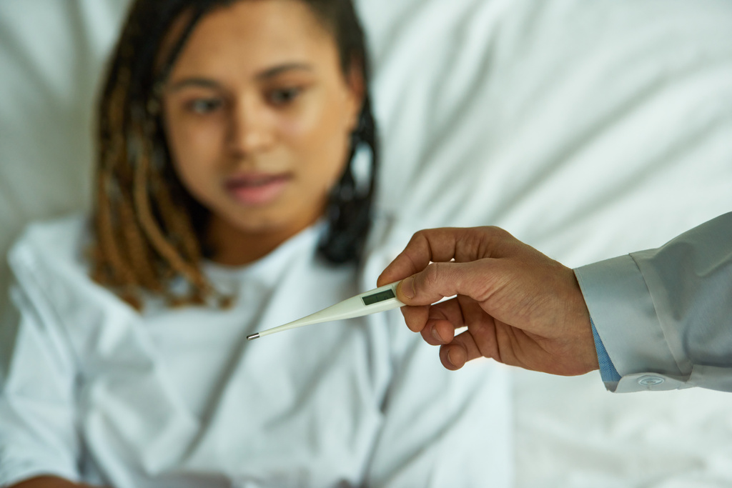 doctor sosteniendo termómetro cerca de mujer afroamericana, sala privada, hospital, síntomas, enfermedad - Foto, Imagen