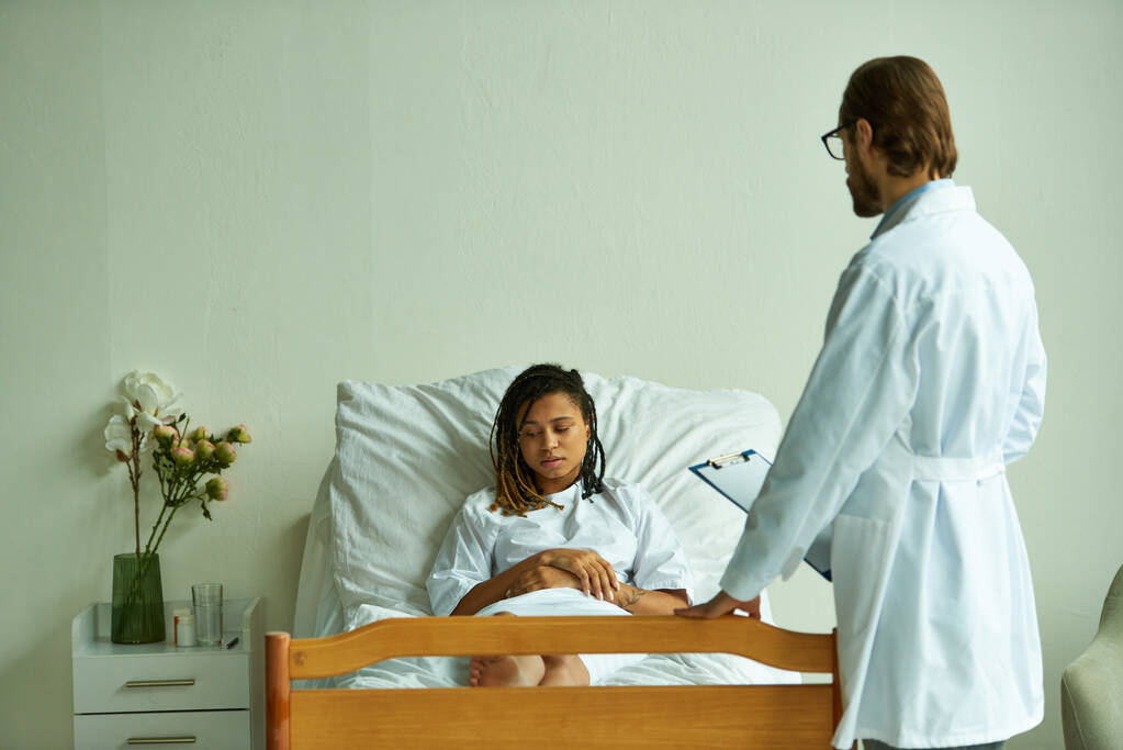 Arzt steht mit Klemmbrett in der Nähe von Afroamerikanerin, Privatstation, Krankenhaus, Konsultation - Foto, Bild