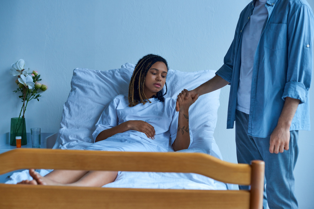 aborto espontâneo, homem chateado segurando a mão da triste esposa afro-americana, dor, cama de hospital, enfermaria privada - Foto, Imagem