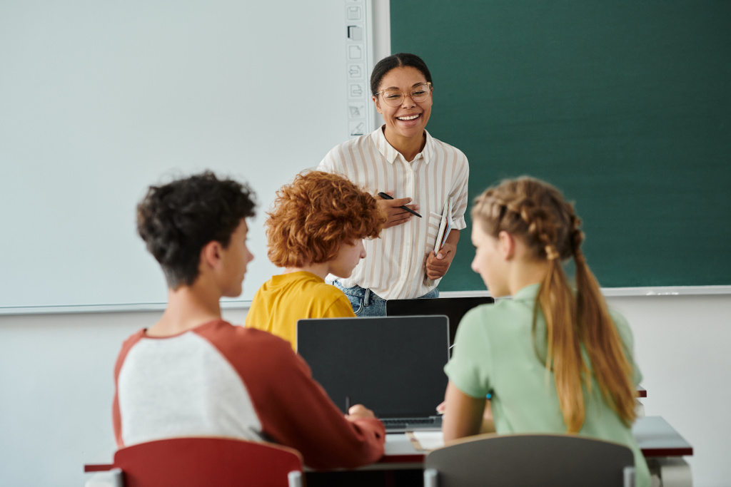 Professeur afro-américain tenant un cahier près des élèves avec des appareils pendant les cours en classe à l'école - Photo, image