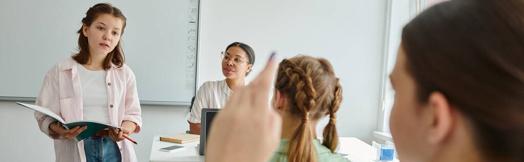 Studentessa che tiene il taccuino vicino all'insegnante afro-americano e compagna di classe con mano sollevata, striscione - Foto, immagini