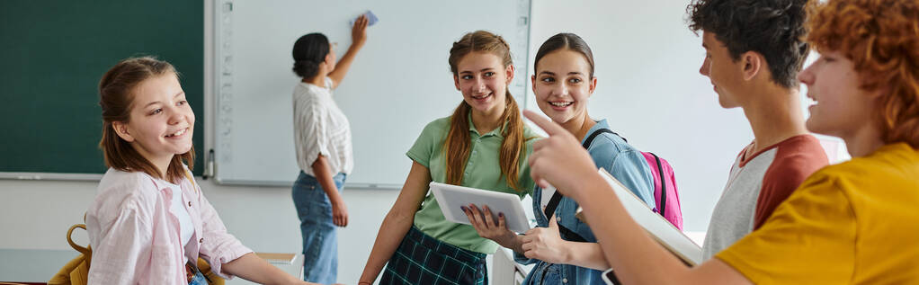 Écoliers parlant et pointant vers des amis proches et professeur afro-américain flou en classe, bannière - Photo, image