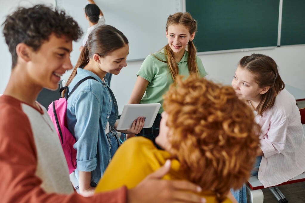 Alunos adolescentes alegres conversando e usando tablet digital perto de amigos desfocados em sala de aula na escola - Foto, Imagem
