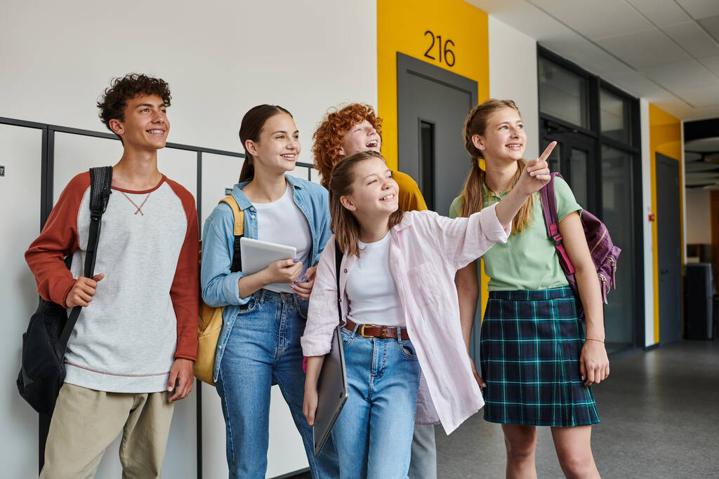 boldog tini diákok néz félre az iskola folyosóján, iskolás lány mutogatott ujjal el, osztálytársak - Fotó, kép