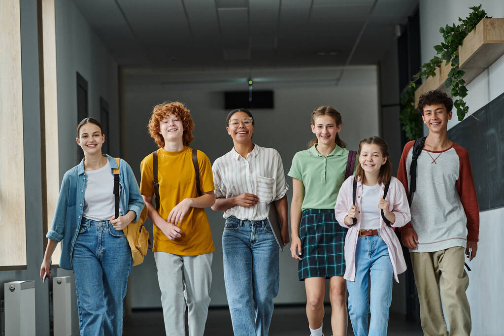 vissza az iskolába, kulturális sokszínűség, boldog tanár és tinédzser diákok sétálnak az iskola folyosóján - Fotó, kép