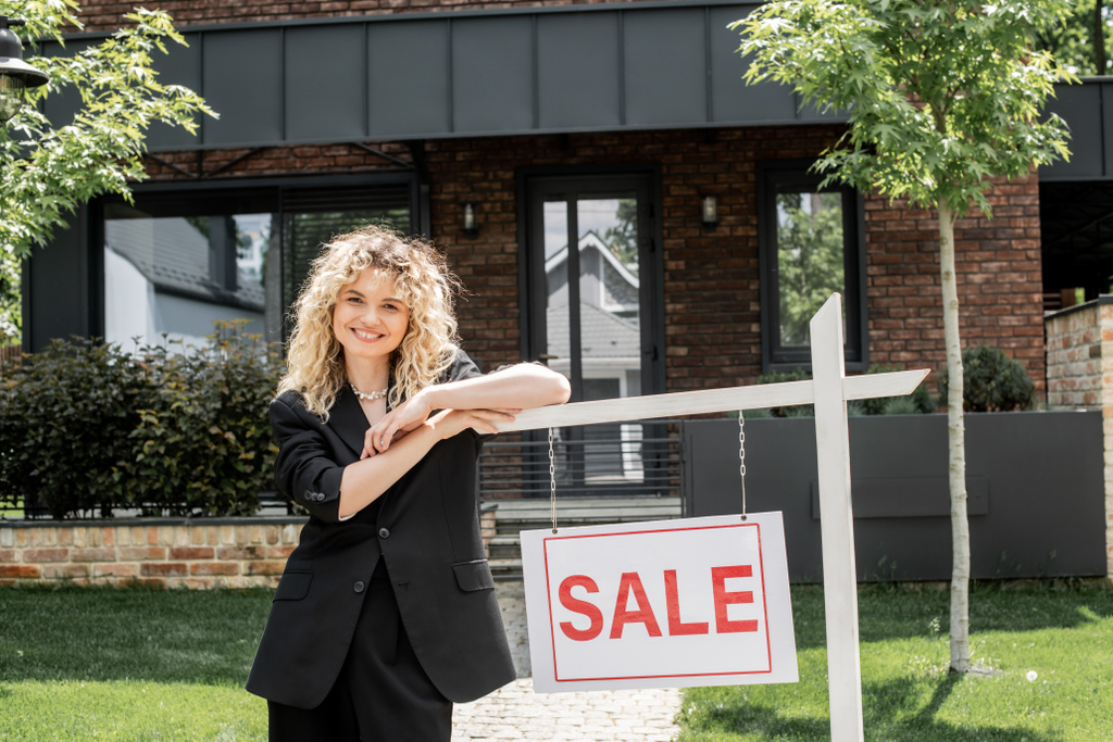 Vidám szőke ingatlanügynök áll közel eladó tábla mellett ház - Fotó, kép