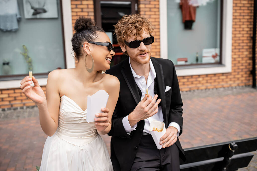 mariage en plein air, snacking, couple interracial élégant, tenue élégante, lunettes de soleil, frites - Photo, image