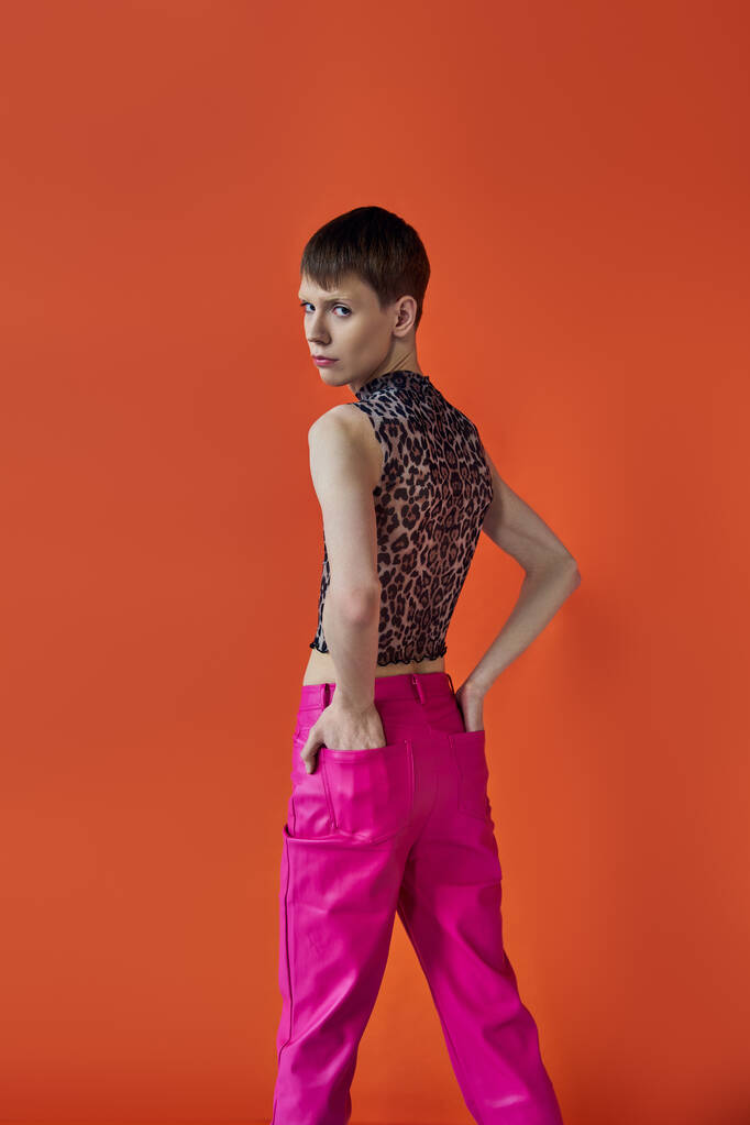 moda queer, persona no binaria posando con las manos en bolsillos de pantalones de color rosa, animal print, patrón - Foto, Imagen