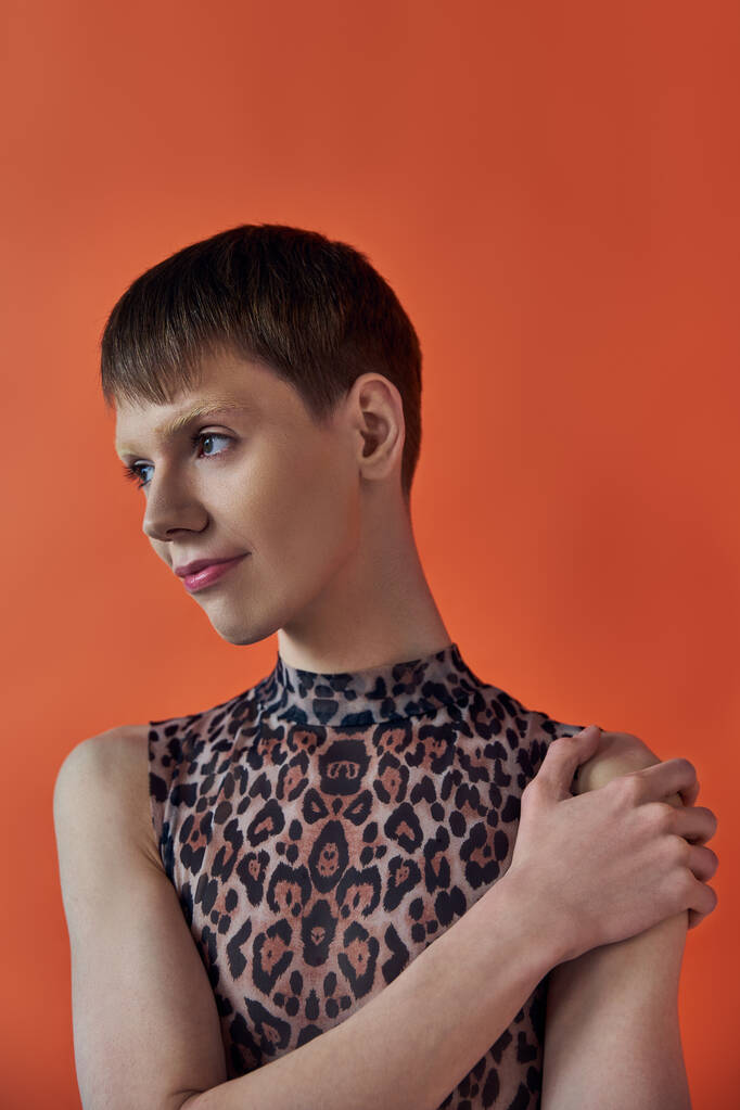 queere Mode, fröhliche nichtbinäre Person, die lächelt und wegsieht, orangefarbener Hintergrund, Animal Print - Foto, Bild