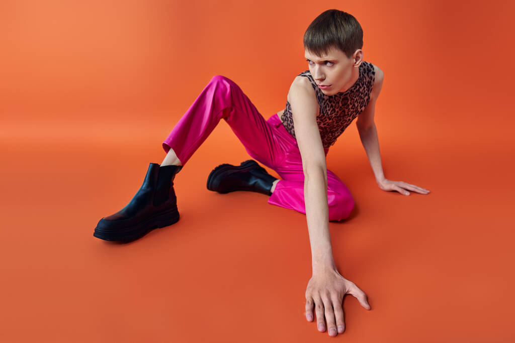 persona queer in top stampa leopardo e pantaloni rosa seduta su sfondo arancione, stile e moda - Foto, immagini