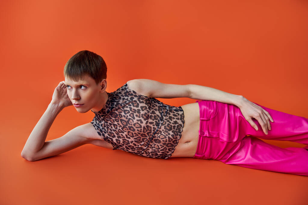 オレンジ色の背景,スタイル,ファッションに横たわるヒョウのプリントトップとピンクのズボン - 写真・画像