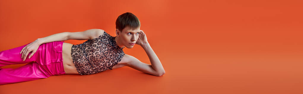 queer person in leopard print top and pink pants lying on orange backdrop, style and fashion, banner - Photo, Image