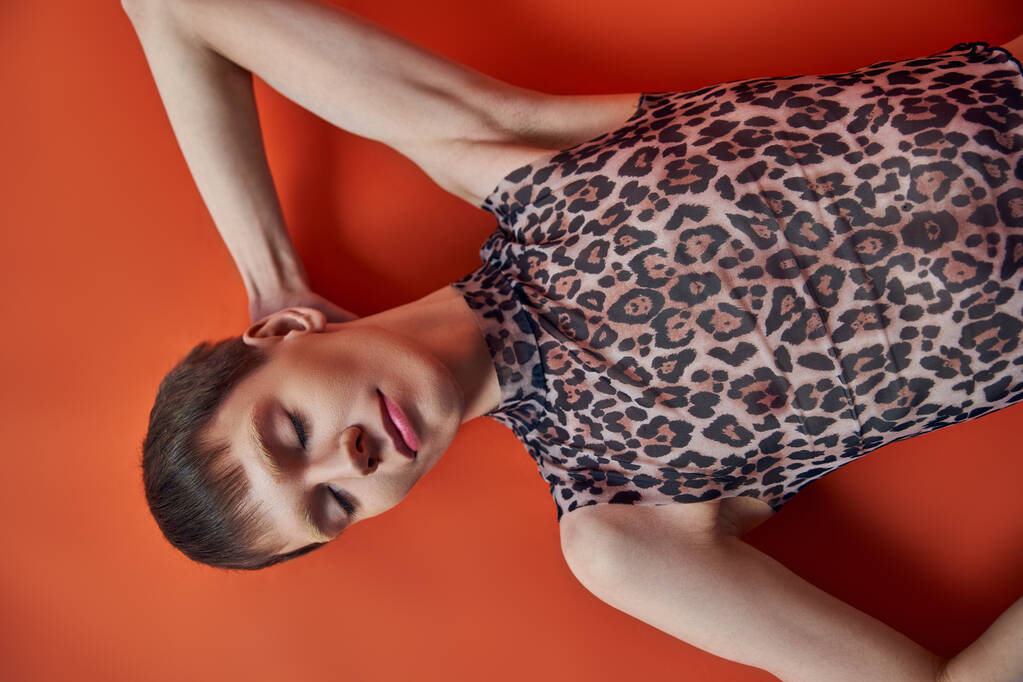 queer person in leopard print sleeveless top lying on orange backdrop, top view, style and fashion - Photo, Image