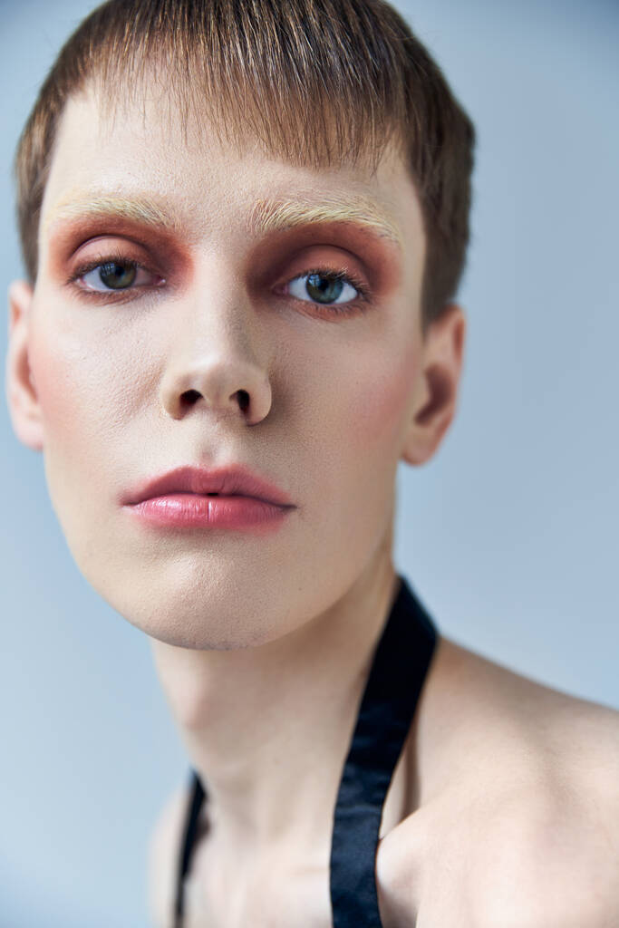 close-up, androgyne persoon met make-up, grijze achtergrond, schoonheid en gezicht, queer, kijk naar de camera - Foto, afbeelding