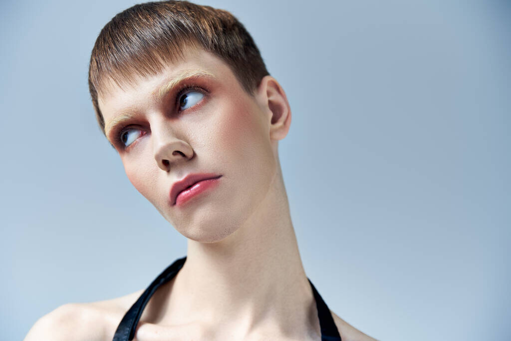 portret, androgynamiczny model z makijażem odwracającym wzrok na szarym tle, piękno i twarz, queer - Zdjęcie, obraz