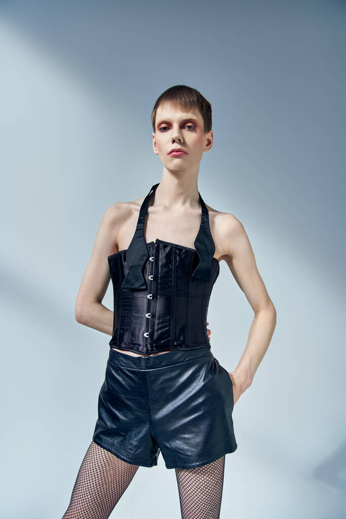teplý model v černém korzetu a šortky pózující na šedém pozadí, androgynní, ruka v kapse - Fotografie, Obrázek