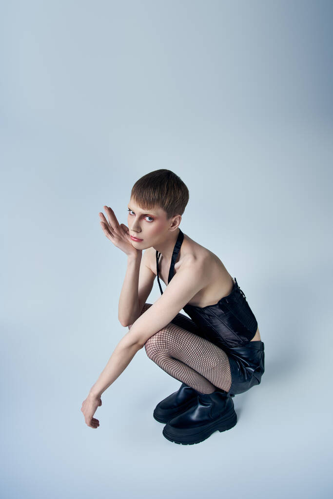 модель в черном корсете и шорты сидя на сером фоне, андрогинный человек, странная мода - Фото, изображение