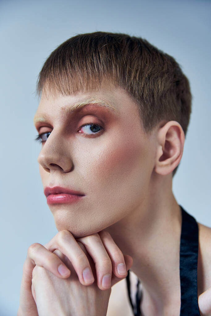 queer model z makijażem patrzący w kamerę na szarym tle, androgynous person, portret, tożsamość - Zdjęcie, obraz