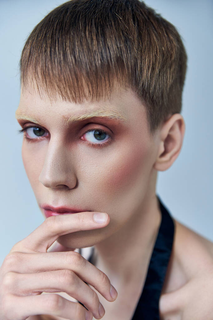 queere Person mit Make-up, die vor grauem Hintergrund wegschaut, androgyne Person, Porträt, Identität - Foto, Bild