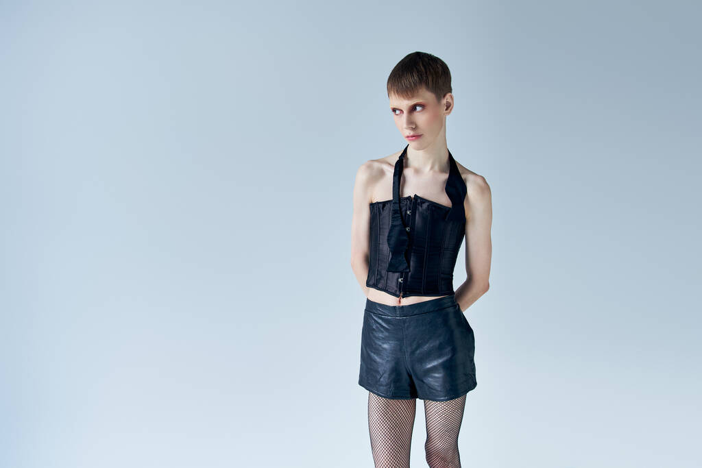 modèle androgyne en corset noir et short regardant loin sur gris, lgbt, mode queer, style - Photo, image