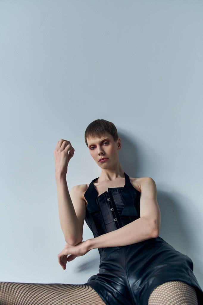 androgynes Modell in Korsett, Shorts und Netzstrumpfhosen posiert vor grauem Hintergrund, queere Mode, lgbtq - Foto, Bild