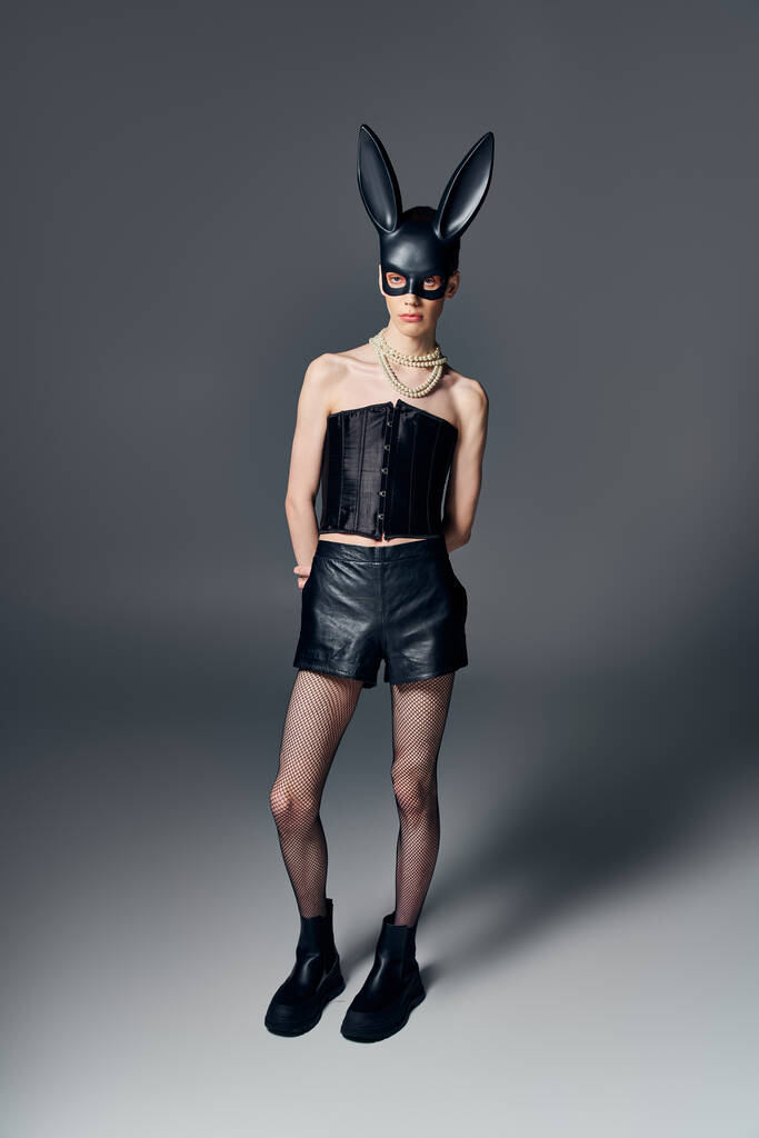 androgynní model v černém korzetu pózující v bdsm králičí masce na šedém pozadí, podivná móda, lgbt - Fotografie, Obrázek