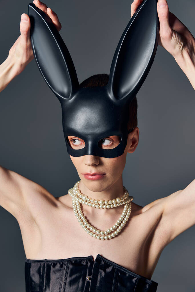 buzerant v korzetu dotýkající se bdsm králičí masky na šedé, perleťový náhrdelník, lgbtq, androgynní - Fotografie, Obrázek