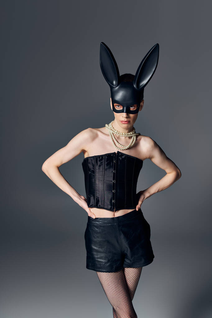 moda, pessoa genderqueer em espartilho posando em bdsm máscara de coelho em cinza, estilo queer, mãos em quadris - Foto, Imagem