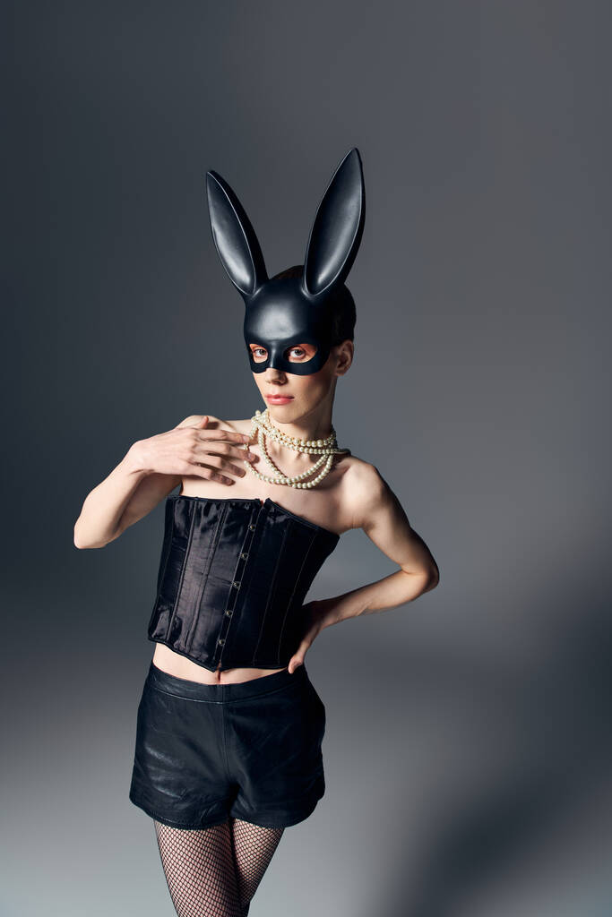 мода, гендерна рідина людина в корсеті позує в бджільницькій масці кролика на сірому, квір-стилі, рука на стегні - Фото, зображення