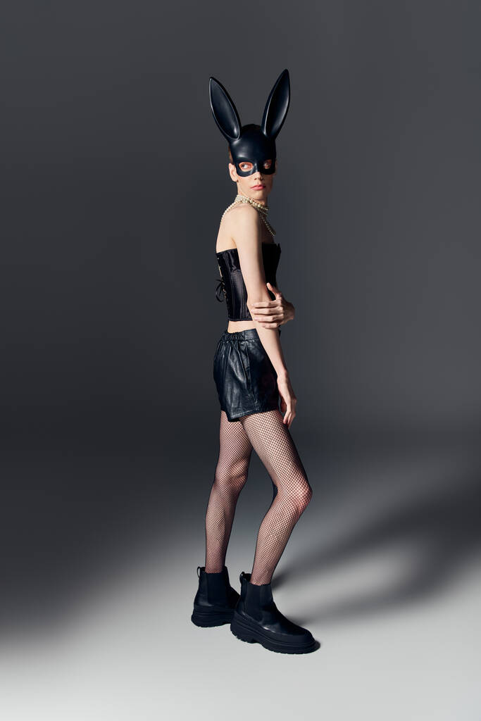 gender fluid person in bold outfit posing in bdsm bunny mask on grey, queer fashion, full length - Photo, Image