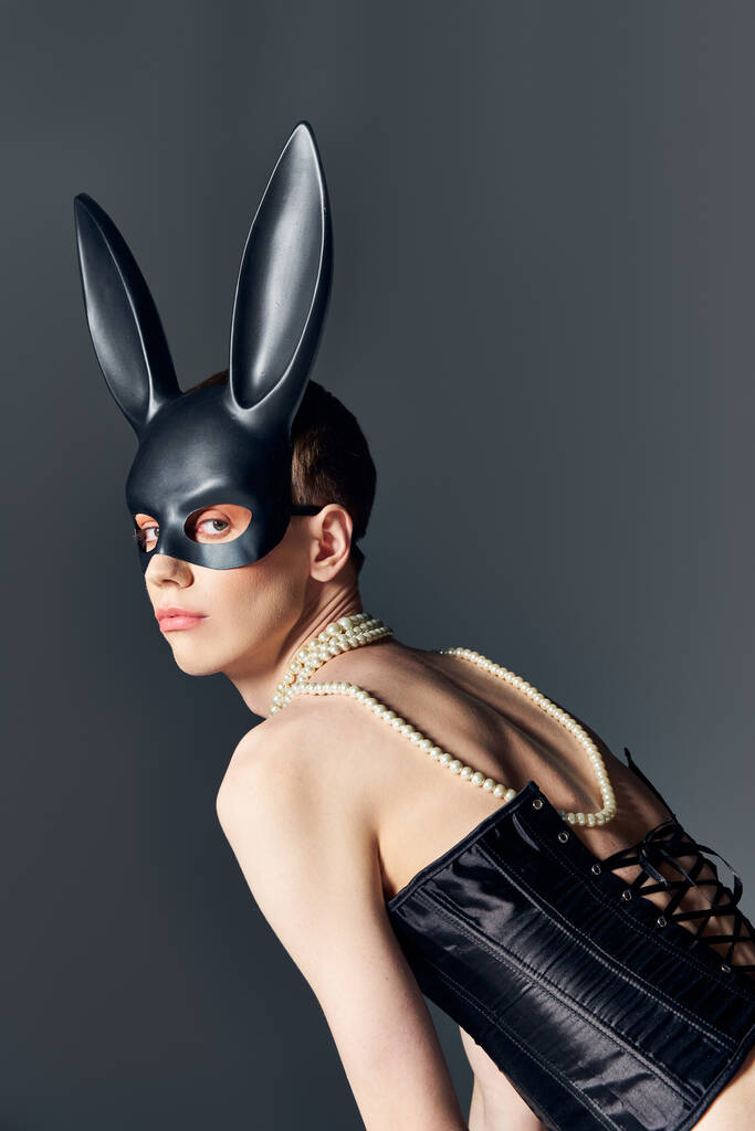 queer persona en negro corsé y bdsm conejito máscara posando en gris, corsé de cordones, moda vanguardista - Foto, Imagen