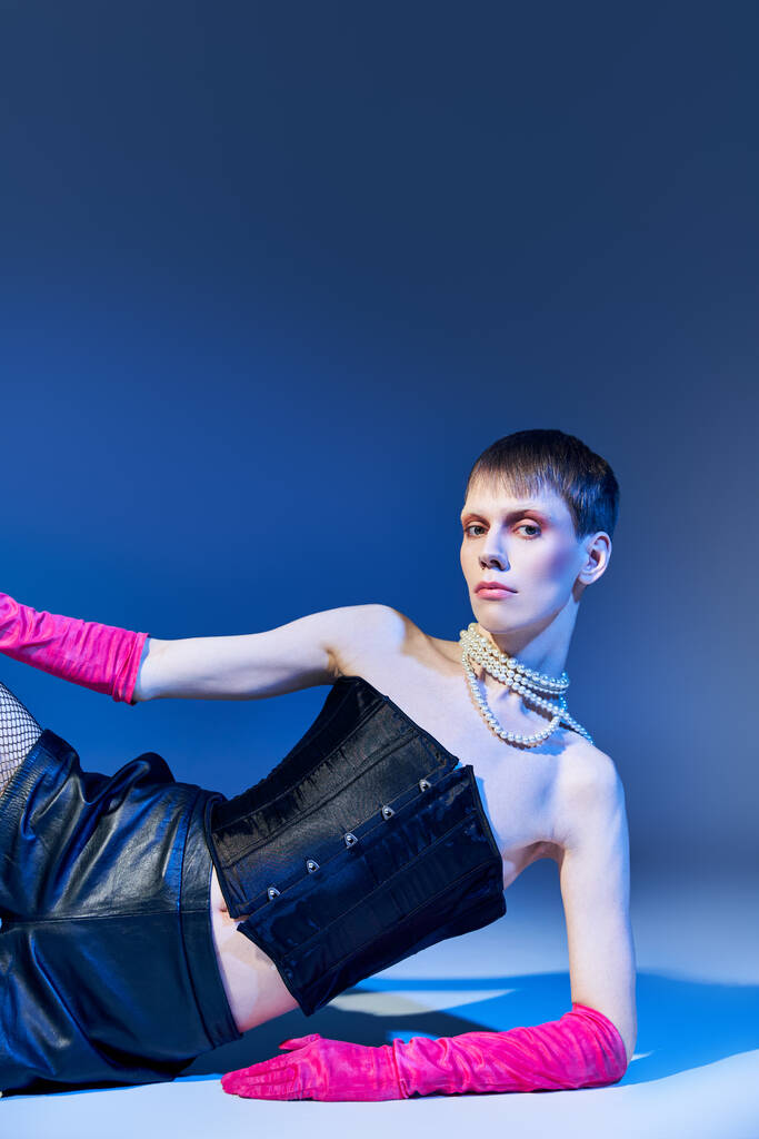 modèle queer en tenue audacieuse et gants roses posant sur fond bleu, short, non binaire, style - Photo, image