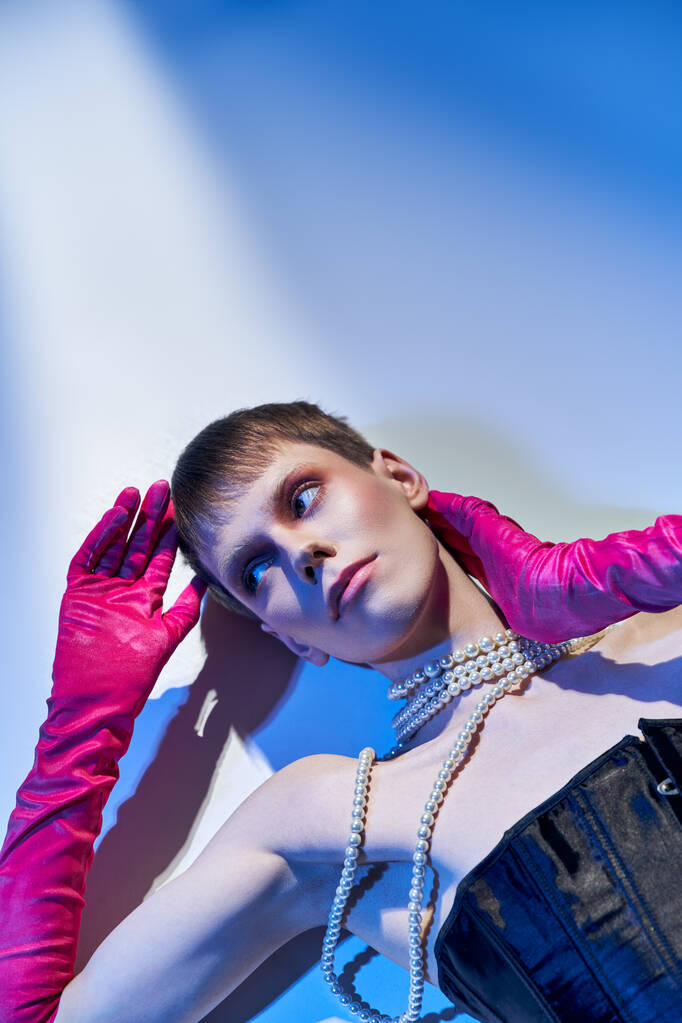 vista superior, modelo genderqueer en corsé y guantes de color rosa mirando hacia otro lado y acostado sobre fondo azul, lgbt - Foto, Imagen