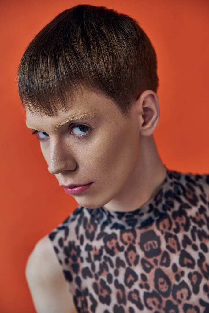 Nahaufnahme eines queeren Models im Animal-Print-Outfit, das auf orangefarbenem Hintergrund posiert und in die Kamera blickt - Foto, Bild