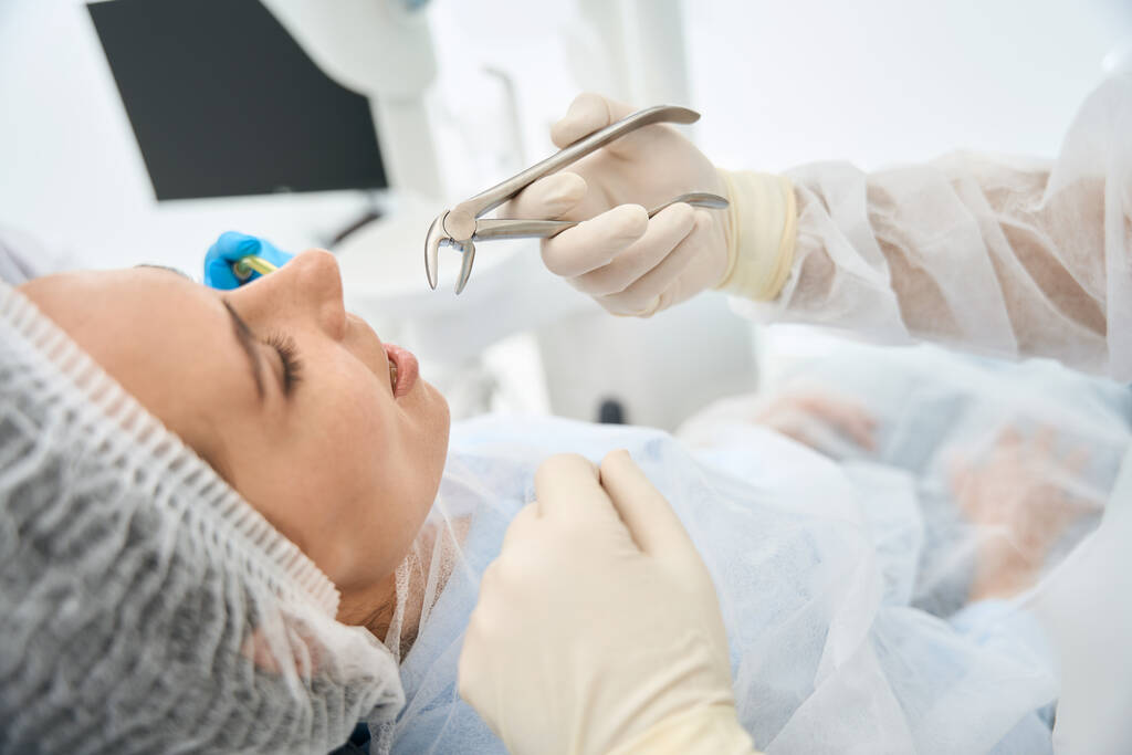 Młoda pacjentka na krześle dentystycznym na ekstrakcji zęba, dentysta używa specjalnych kleszczy - Zdjęcie, obraz