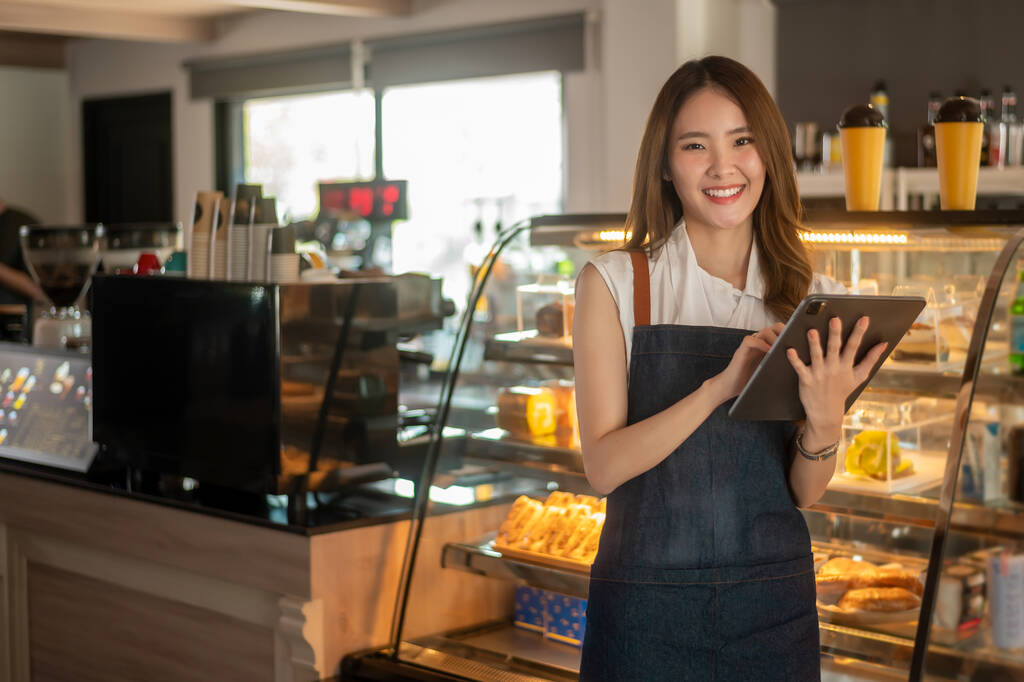 Eine asiatische Unternehmerin, die Tablette benutzt, um Aktien oder Verkaufserlöse in einem modernen Coffeeshop zu überprüfen, Konzept Kleinunternehmen  - Foto, Bild