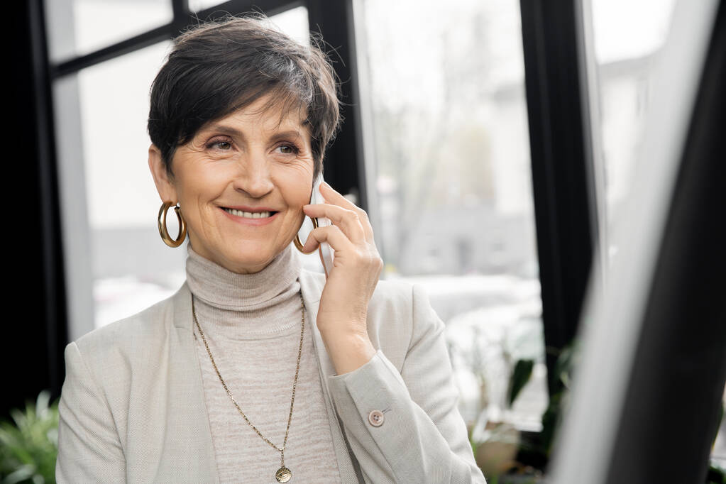 Modern ofiste gülümseyen ve akıllı telefondan konuşan orta yaşlı girişimci, iş başarısı - Fotoğraf, Görsel
