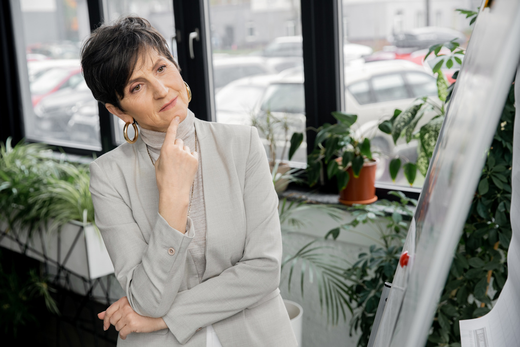 pensativa mujer de negocios de mediana edad mirando el rotafolio borroso en la oficina, toma de decisiones - Foto, imagen