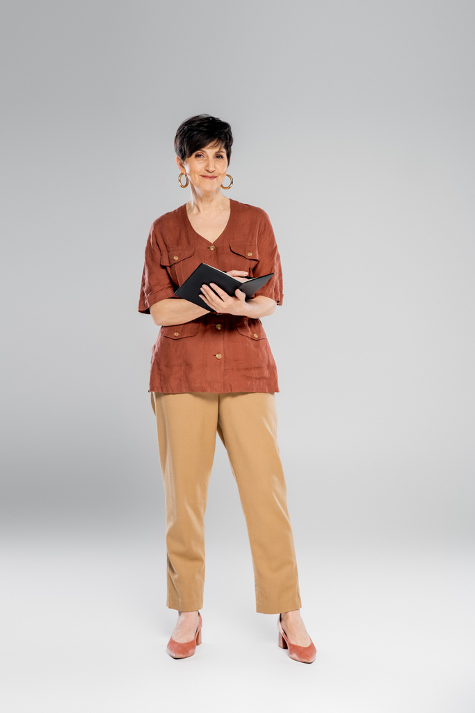 trendige Geschäftsfrau mit Notizbuch auf grau, Herbst, Saisonmode, braune Jacke, beige Hose - Foto, Bild