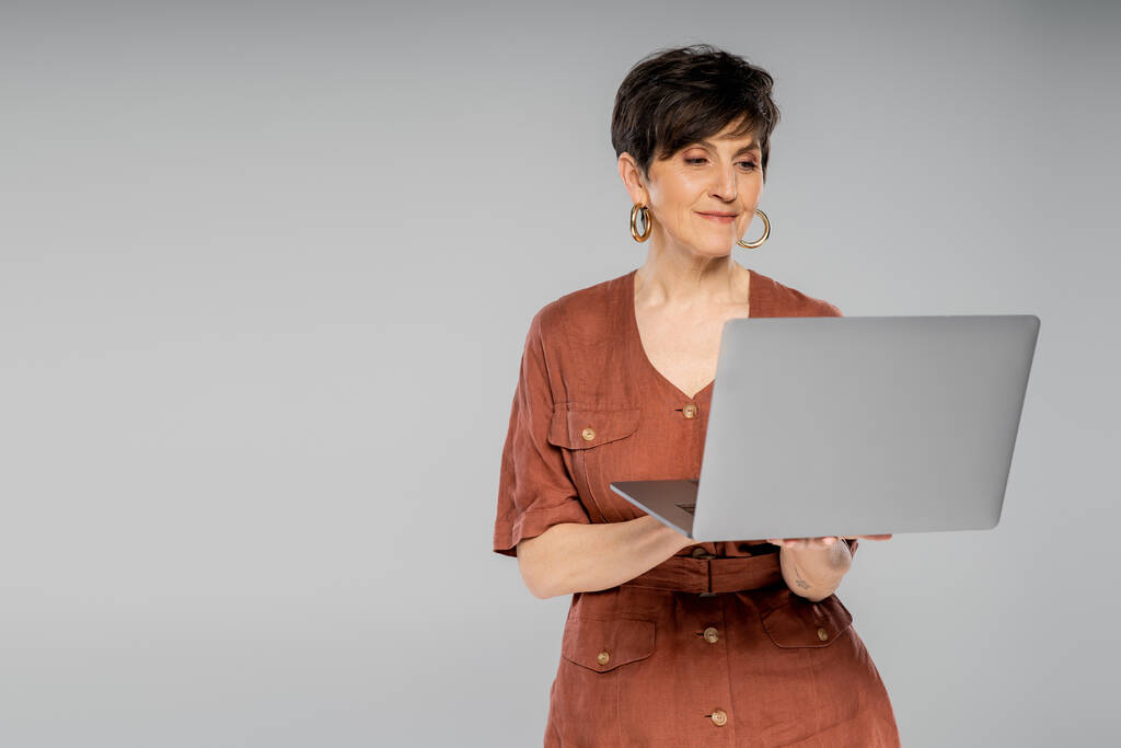 mulher de negócios de meia idade em casaco marrom trabalhando no laptop em cinza, look de outono na moda - Foto, Imagem
