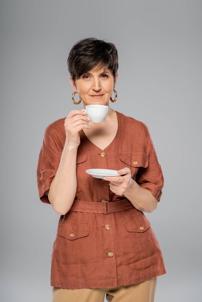 brünette Frau mittleren Alters in brauner Leinenjacke, Kaffee trinkend auf grau, Herbstmode - Foto, Bild
